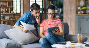 Young couple sitting on sofa reviewing documents on a tablet